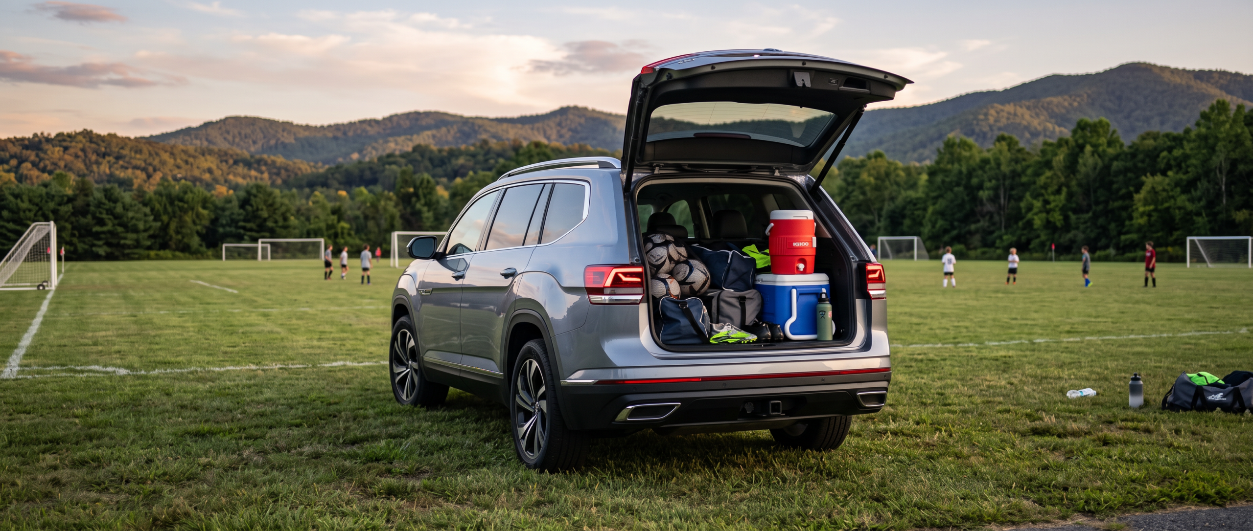 2026 Volkswagen Atlas rear liftgate open at a Spartanburg youth soccer field with gear bags loaded, Blue Ridge foothills in the background